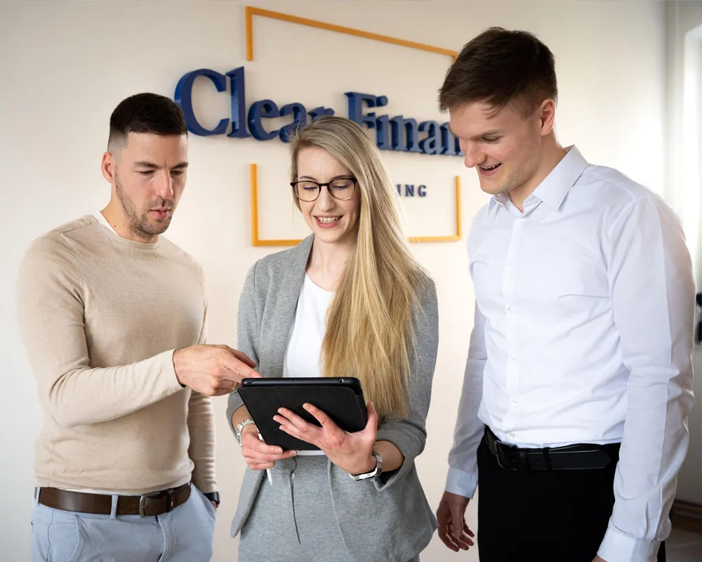 Sabrina, Rick und Aron im Empfangsbereich von Clear Finance, gemeinsam auf ein iPad blickend, mit dem Clear Finance Logo im Hintergrund.“