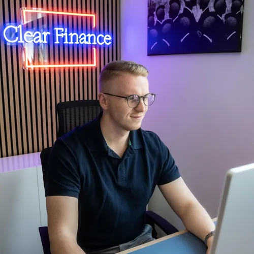 Sascha Leuthold sitzend am Schreibtisch mit de Clear Finance Logo im Hintergrund
